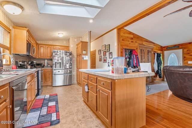 kitchen featuring tile countertops, appliances with stainless steel finishes, open floor plan, a sink, and vaulted ceiling with skylight