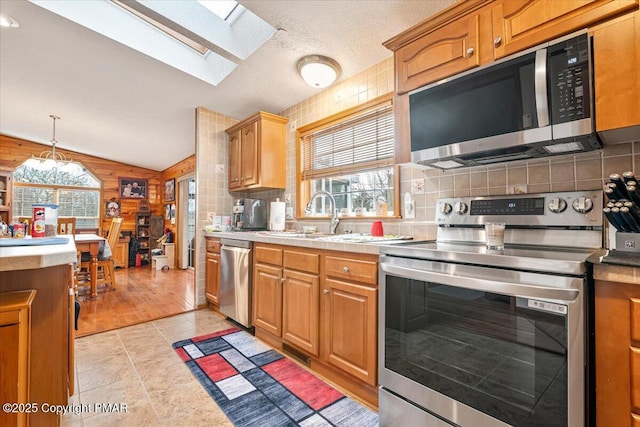 kitchen featuring tasteful backsplash, vaulted ceiling, stainless steel appliances, wood walls, and a sink