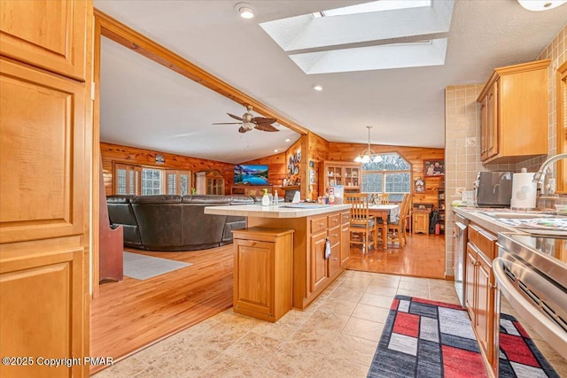 kitchen featuring vaulted ceiling with skylight, wooden walls, a kitchen island, light countertops, and a sink