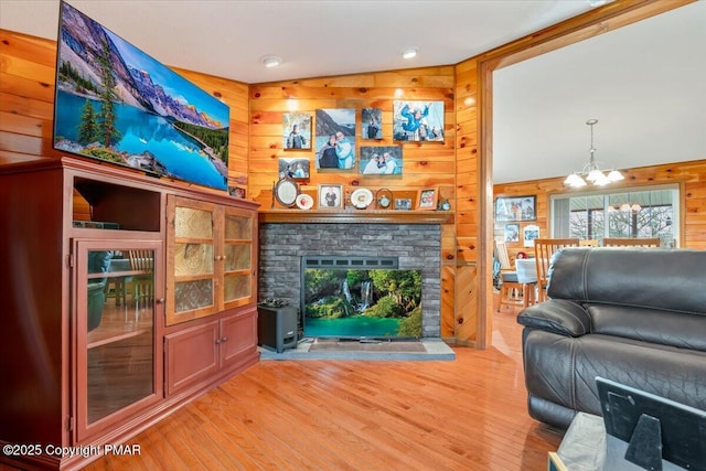 living area with wood walls, a fireplace, light wood-style flooring, and a notable chandelier