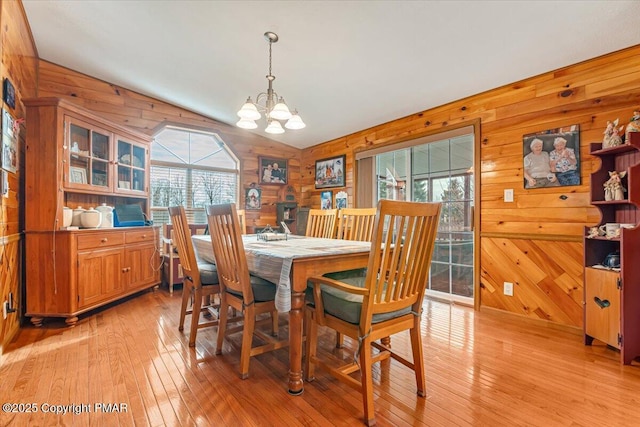 dining area with a chandelier, lofted ceiling, wooden walls, and light wood finished floors