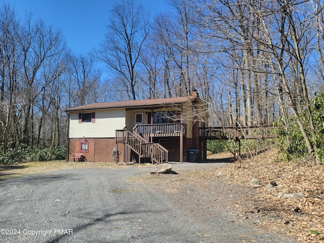 view of front of house featuring stairs, driveway, a deck, and a chimney