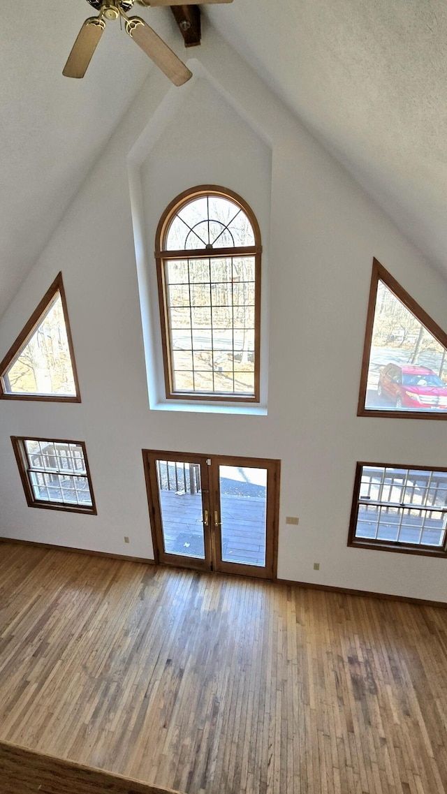 unfurnished living room with hardwood / wood-style flooring, high vaulted ceiling, french doors, and ceiling fan