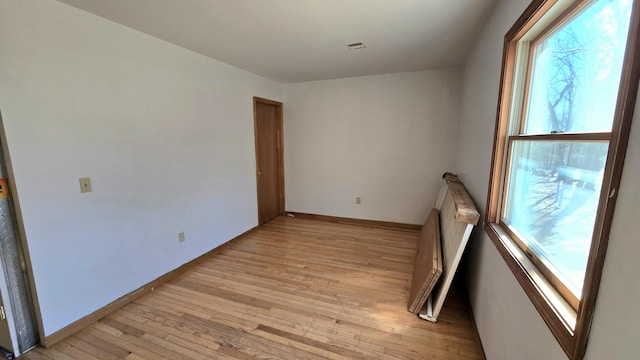 empty room featuring visible vents, light wood-type flooring, and baseboards