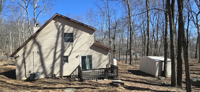 view of side of home featuring a wooden deck, cooling unit, a chimney, an outbuilding, and a storage unit