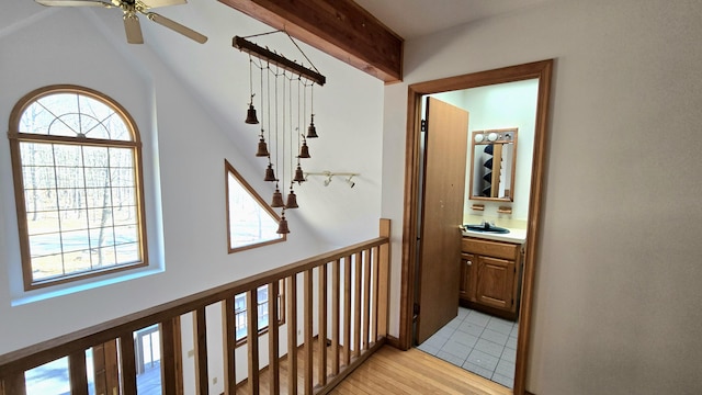 corridor with a healthy amount of sunlight, lofted ceiling with beams, light wood-style floors, and a sink