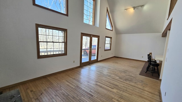 unfurnished living room featuring french doors, wood-type flooring, baseboards, and a towering ceiling