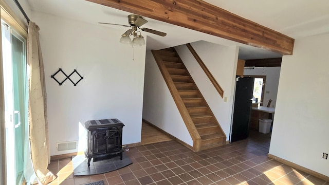 unfurnished living room featuring stairway, visible vents, a wood stove, dark tile patterned flooring, and beamed ceiling