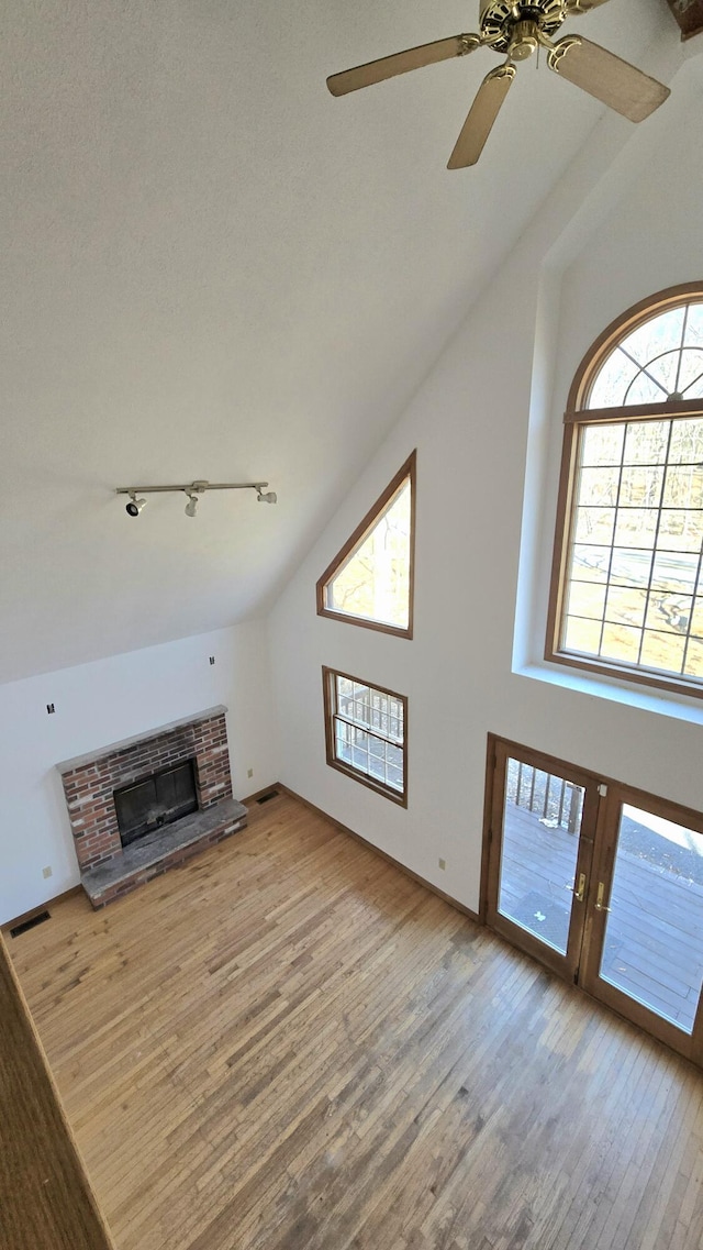 unfurnished living room with plenty of natural light, a brick fireplace, a ceiling fan, and wood-type flooring