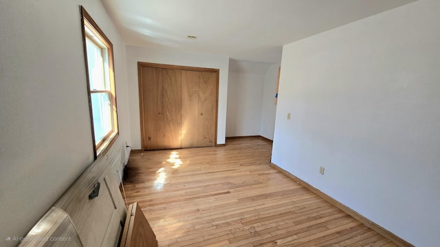 unfurnished bedroom with a closet, arched walkways, baseboards, and light wood finished floors