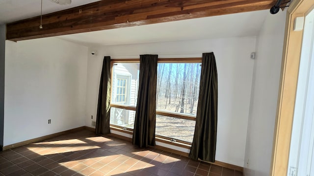 unfurnished room with a wealth of natural light, beamed ceiling, dark tile patterned floors, and baseboards