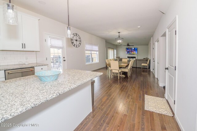 kitchen featuring dark wood-type flooring, light stone counters, decorative light fixtures, stainless steel dishwasher, and white cabinets