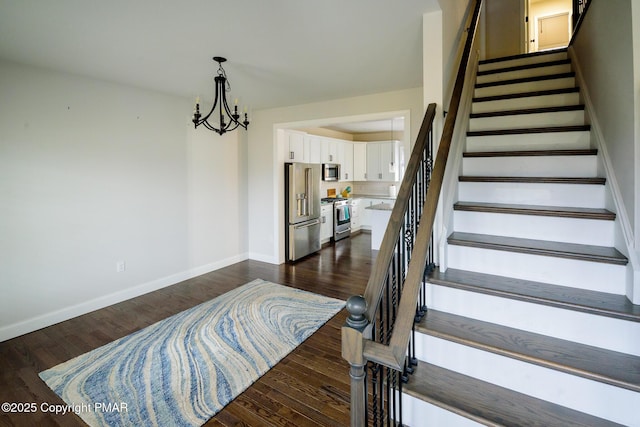 stairway with a notable chandelier, baseboards, and wood finished floors