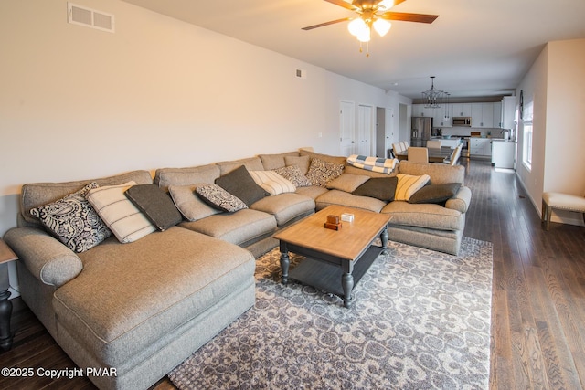 living room with ceiling fan with notable chandelier, visible vents, and dark wood-style flooring