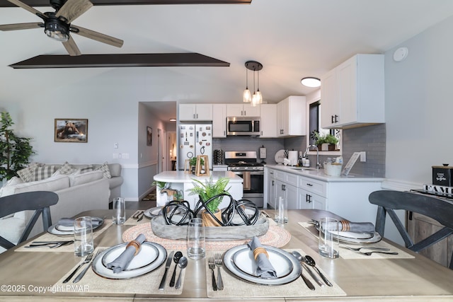 dining space featuring ceiling fan, vaulted ceiling with beams, and sink