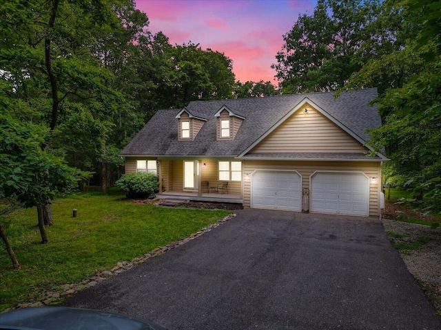 new england style home featuring a yard, a shingled roof, covered porch, an attached garage, and driveway