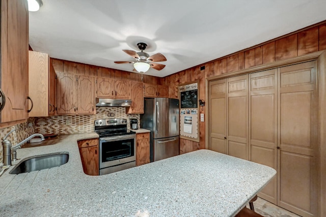 kitchen featuring decorative backsplash, appliances with stainless steel finishes, a peninsula, under cabinet range hood, and a sink