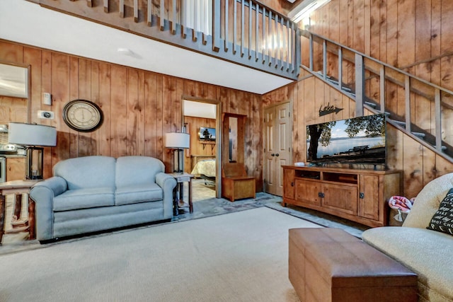 carpeted living area with wooden walls, stairway, and a high ceiling