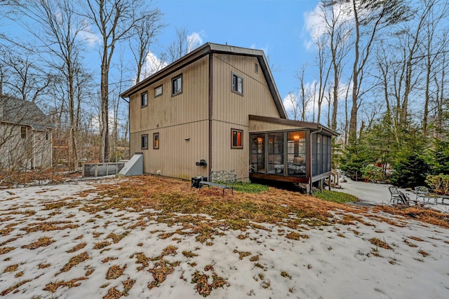 snow covered rear of property with a sunroom