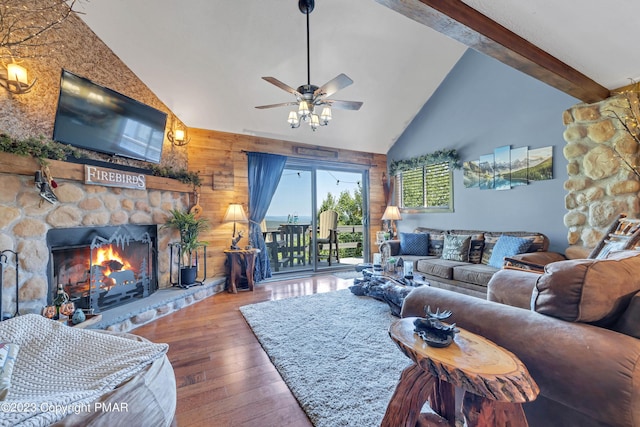 living area with beam ceiling, a stone fireplace, wooden walls, high vaulted ceiling, and hardwood / wood-style flooring