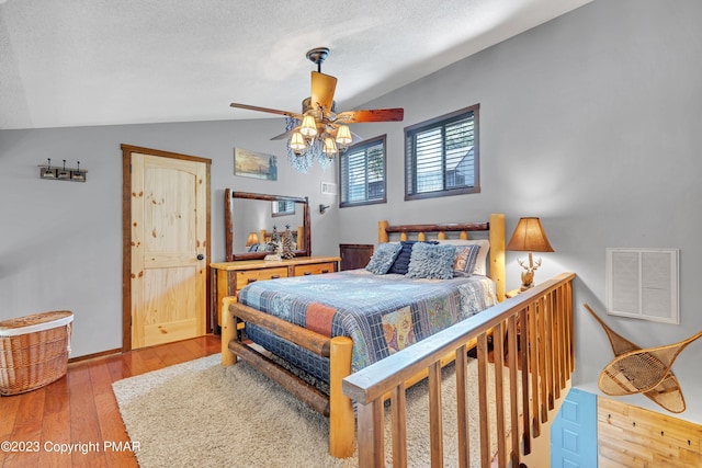 bedroom featuring wood-type flooring, visible vents, vaulted ceiling, a textured ceiling, and ceiling fan