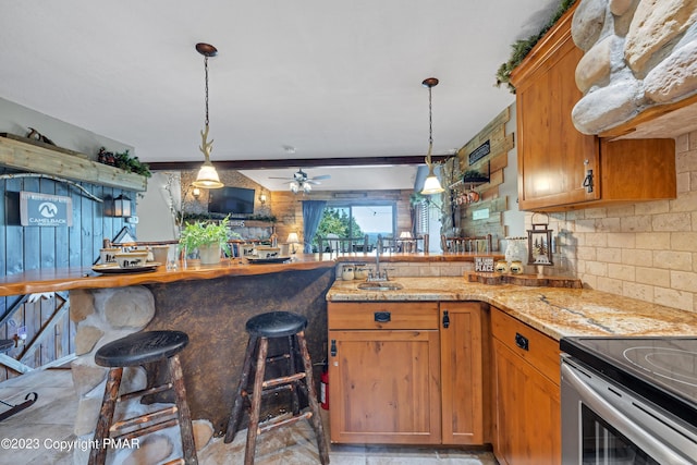 kitchen featuring decorative light fixtures, a sink, a peninsula, and light stone countertops