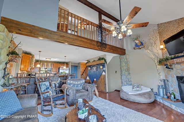 living room with wood-type flooring, stairway, ceiling fan, a stone fireplace, and beamed ceiling