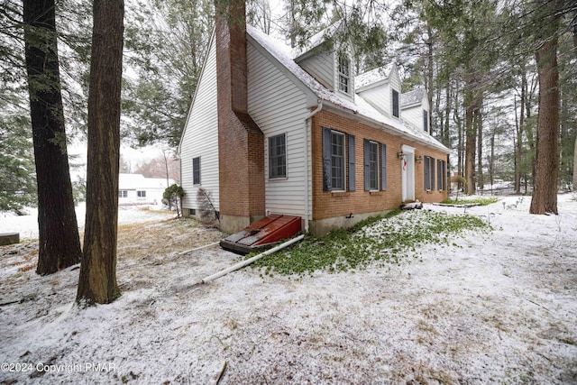 view of snow covered exterior with a chimney and brick siding