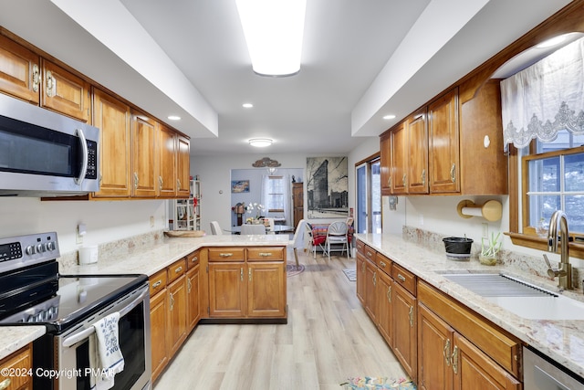 kitchen with appliances with stainless steel finishes, brown cabinetry, a sink, and light wood-style flooring