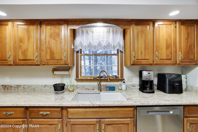 kitchen with dishwasher, light stone counters, brown cabinetry, and a sink