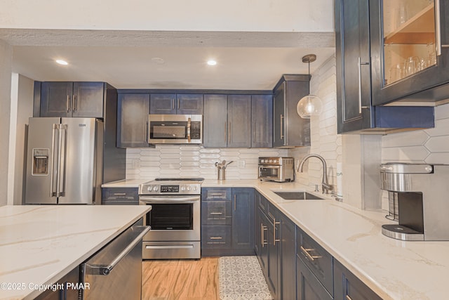 kitchen featuring sink, light stone counters, decorative light fixtures, stainless steel appliances, and decorative backsplash