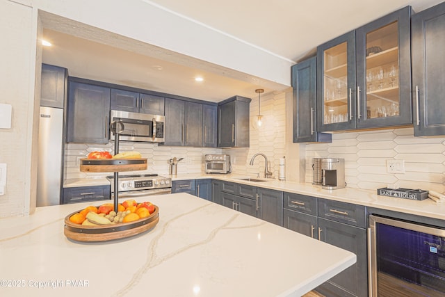 kitchen featuring sink, appliances with stainless steel finishes, hanging light fixtures, light stone counters, and beverage cooler