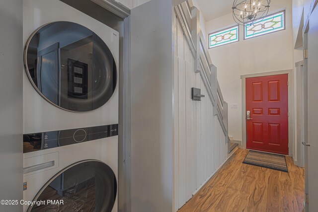 laundry room featuring hardwood / wood-style flooring, a towering ceiling, stacked washer / drying machine, and a chandelier