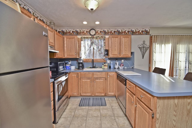 kitchen featuring a sink, under cabinet range hood, recessed lighting, appliances with stainless steel finishes, and a peninsula