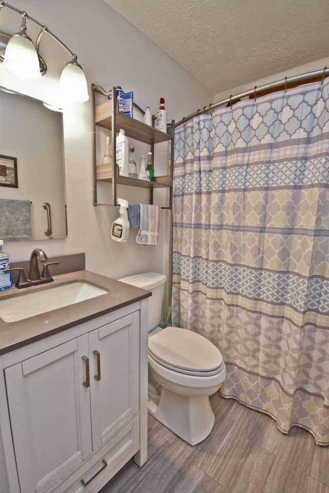 full bathroom with toilet, a textured ceiling, vanity, and wood finished floors