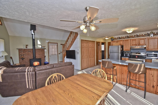 dining space featuring a ceiling fan, a textured ceiling, stairway, light colored carpet, and a wood stove