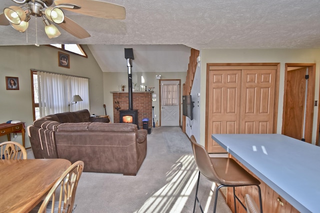 living area featuring ceiling fan, vaulted ceiling, carpet flooring, a wood stove, and a textured ceiling