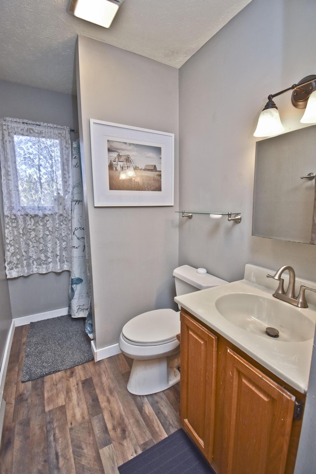 bathroom featuring vanity, wood finished floors, baseboards, a textured ceiling, and toilet