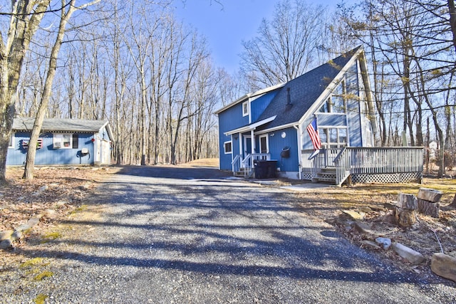 view of side of property with driveway, a shingled roof, and a deck