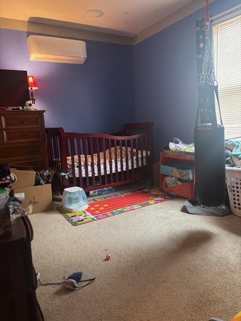 carpeted bedroom featuring a crib and a wall mounted air conditioner