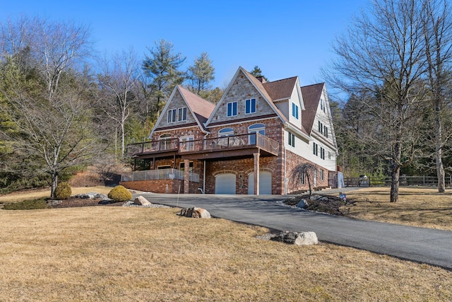 view of front facade featuring aphalt driveway, brick siding, a wooden deck, a garage, and a front lawn