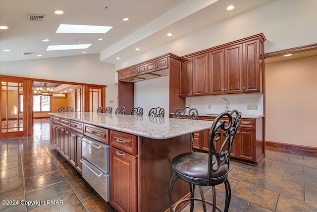 kitchen featuring vaulted ceiling with skylight, a center island with sink, visible vents, a breakfast bar area, and a warming drawer