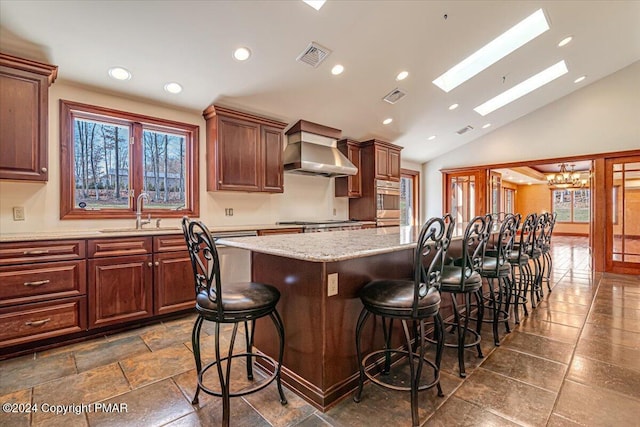 kitchen featuring wall chimney range hood, visible vents, a kitchen breakfast bar, and a sink