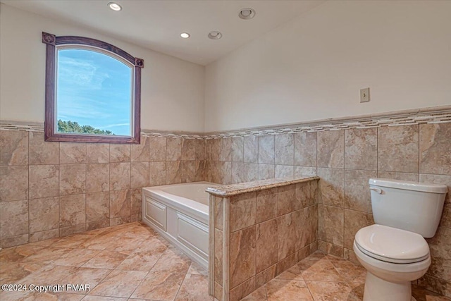 full bath featuring toilet, a wainscoted wall, tile walls, and a bath