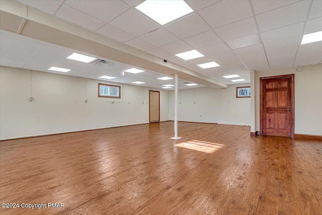 below grade area with wood finished floors, a paneled ceiling, and baseboards