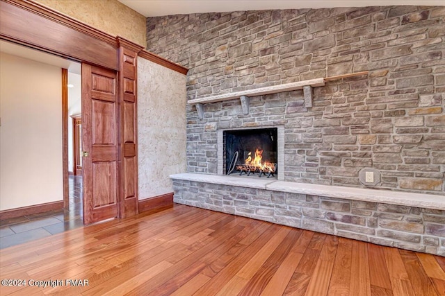 unfurnished living room with a stone fireplace, baseboards, and wood finished floors