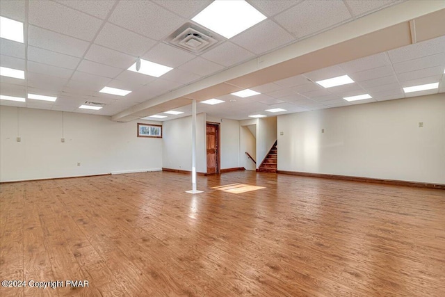 empty room featuring a paneled ceiling, visible vents, stairway, light wood-type flooring, and baseboards