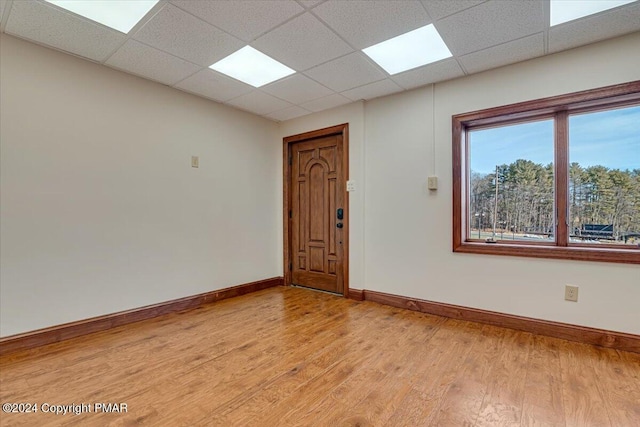 unfurnished room featuring baseboards, a paneled ceiling, and light wood-style floors