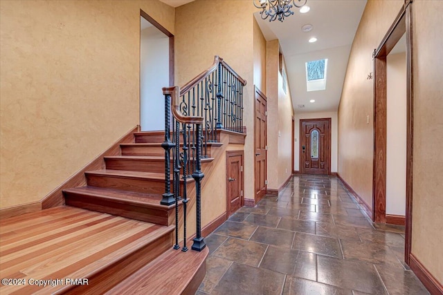 interior space with a chandelier, a skylight, baseboards, stairway, and stone tile flooring