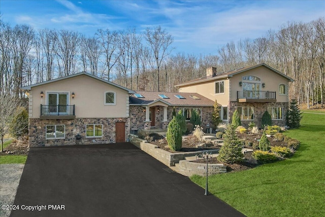 view of front of home with a balcony, stone siding, aphalt driveway, and stucco siding